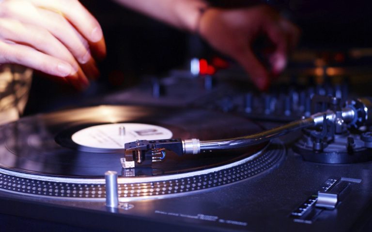 Ein DJ mixt Platten auf einem Turntable mit leuchtenden Reglern.