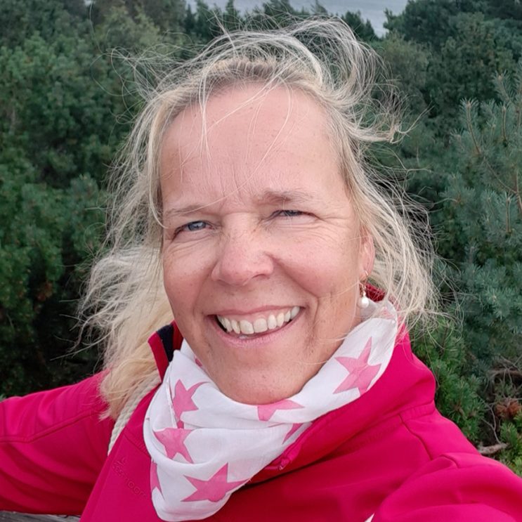 Gemeindesekretärin Angela Händler hat blonde Haare und trägt einen Sternenschal. Sie lächelt vor grüner Landschaft im Hintergrund.