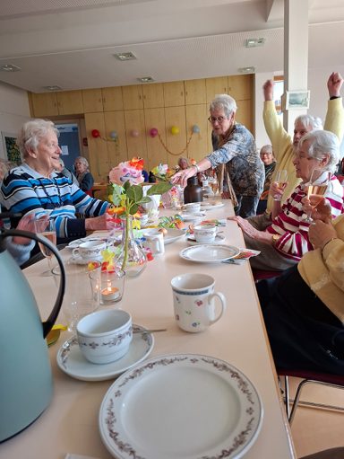 Ältere Menschen sitzen an einem Tisch, genießen ein gemeinsames Kaffeetrinken und unterhalten sich.