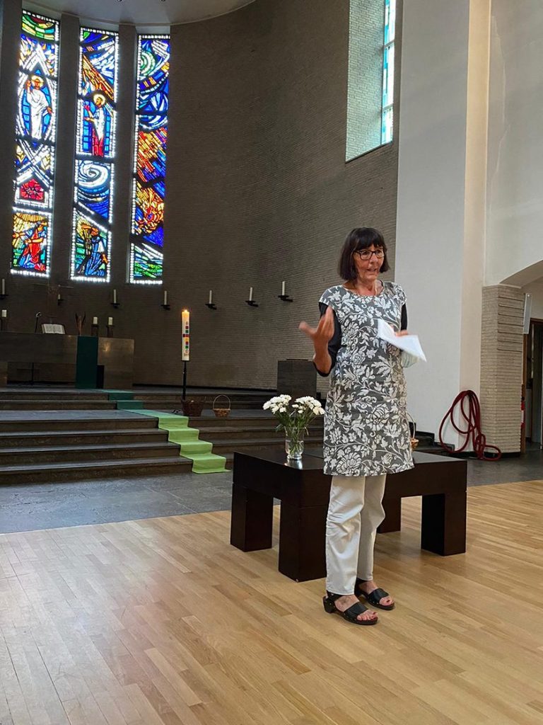 Frau spricht in der Epiphanienkirche, im Hintergrund bunte Kirchenfenster.