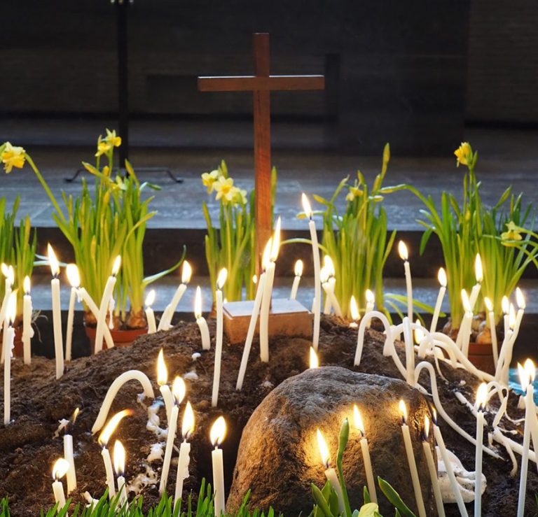Holzkreuz umgeben von brennenden Kerzen und gelben Narzissen in der Epiphanienkirche.