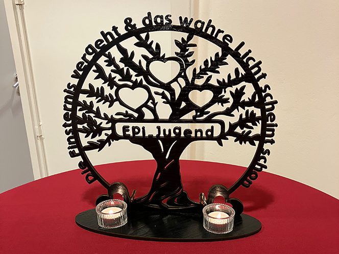 Epiphaniengemeinde Hamburg – Jugendkeller Deko aus Metall mit einem Baum, Herzen und zwei Teelichthaltern auf rotem Tisch.