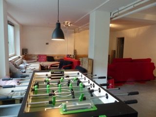 Epiphaniengemeinde Hamburg – Jugendkeller Ein gemütlicher Raum mit Tischfußball, Sofas und natürlichem Licht.