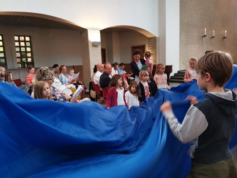 Kinder und Erwachsene halten einen blauen Stoff in der Epiphanienkirche während des Familiengottesdienstes.