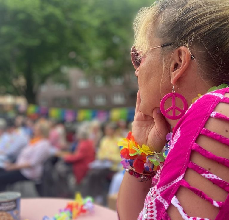 Eine nachdenkliche Person mit bunten Accessoires und Peace-Ohrringen beim Schlager-Gottesdienst vor der Kirche.