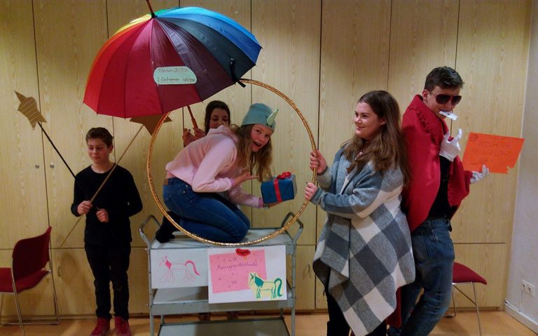 Eine Gruppe von Jugendlichen posiert verkleidet, kreativ mit Requisiten wie einem Regenschirm, einem Hola-Hoop-Reifen und Sternenstäben.