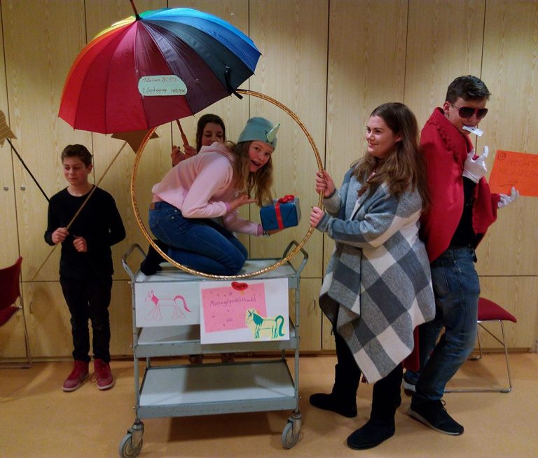 Fünf Teenager posieren mit einem bunten Regenschirm und einem Wagen. Spaßige Gruppenszene.