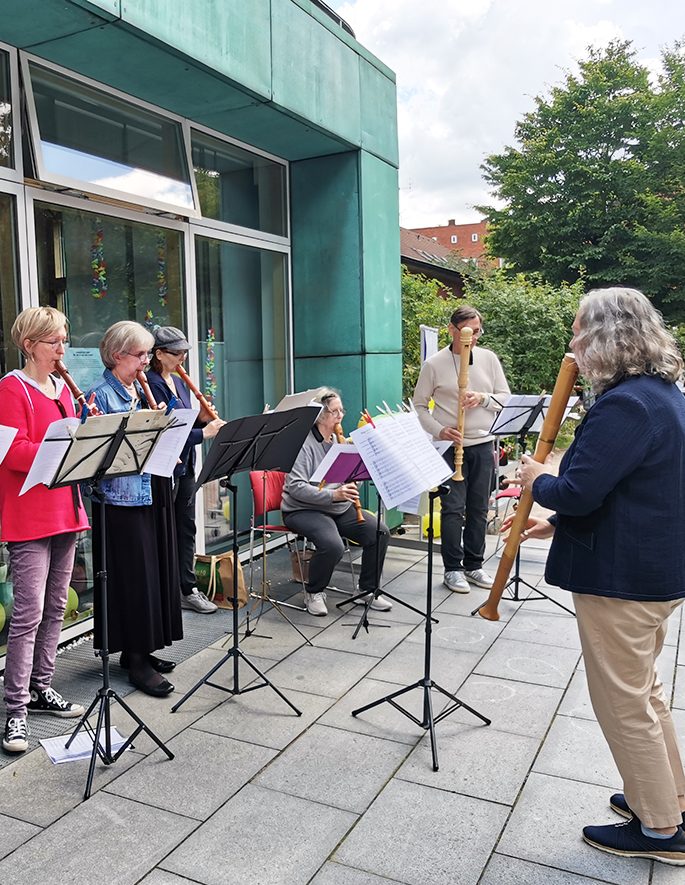 Sechs Musiker*innen spielen verschiedene Flöten im Freien vor der Epiphanienkirche.