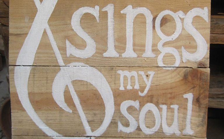 Holzschild mit der Aufschrift 'And sings my soul' in weißen Buchstaben und einem Notenschlüssel.