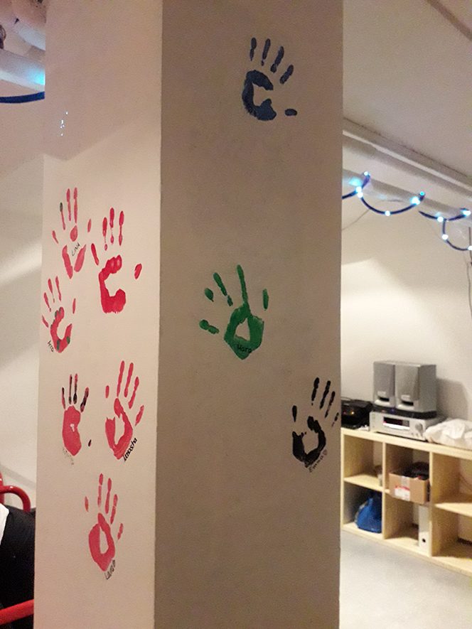 Epiphaniengemeinde Hamburg – Jugendkeller Bunte Handabdrücke in Pink, Grün und Schwarz an einer weißen Wand.