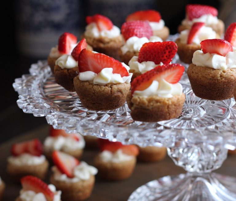 Mini-Törtchen mit Sahne und frischen Erdbeeren auf einem Glasstand.