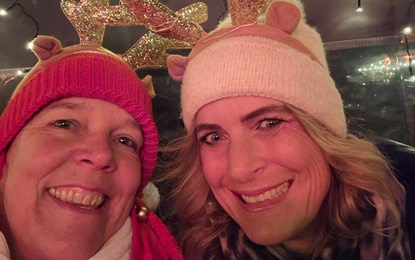 Epiphaniengemeinde Hamburg – Lebendiger Adventskalender Zwei Frauen mit Weihnachtsmützen und Rentiergeweihen, lächelnd in festlicher Atmosphäre.