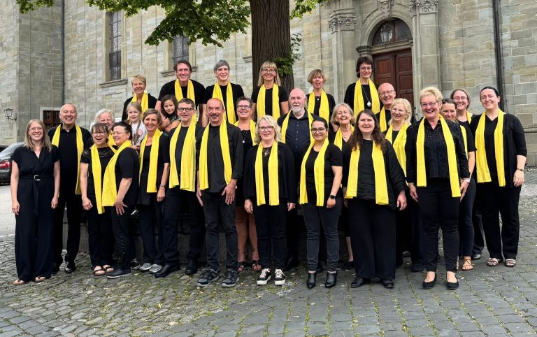 Epiphaniengemeinde Hamburg – Gemeindeversammlung Gospelchor Living Motion steht vor einer Kirche. Alle in Schwarz mit gelben Schals.