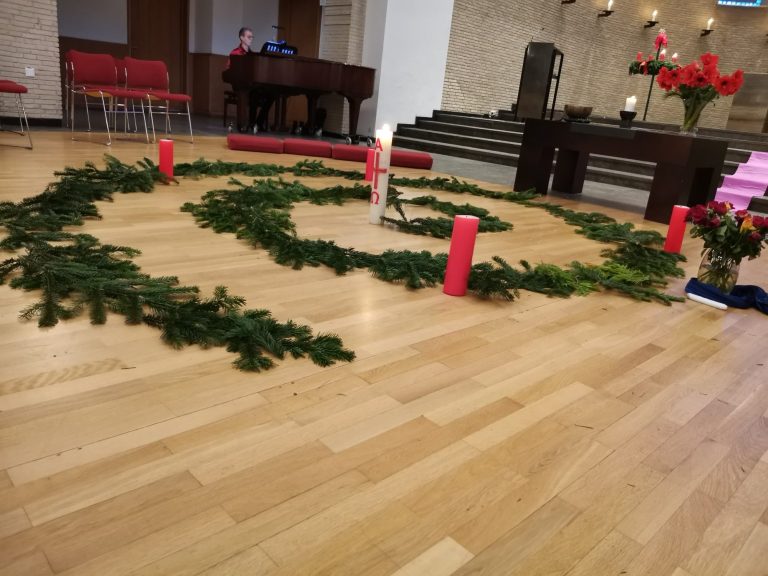 Grüne Tannenzweige und vier rote Kerzen bilden eine Spirale auf dem Boden der Epiphanienkirche.