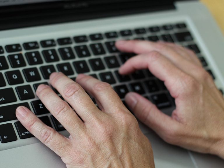 Hände tippen auf einer Laptop-Tastatur.