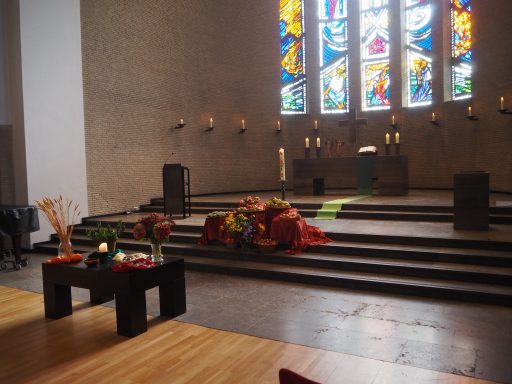 Ein schlichter Kirchenraum mit bunten Fenstern und einer altarähnlichen Bühne.