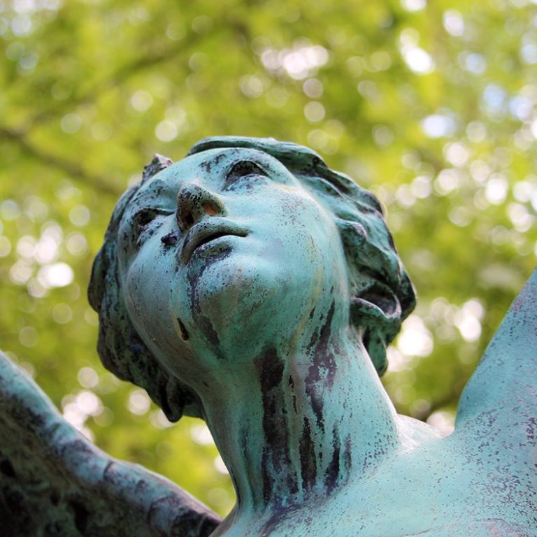Eine Kupferstatue eines Engels mit erhobenem Kopf und ausgebreiteten Flügeln.