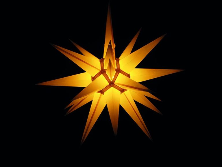 Leuchtender, goldfarbener Weihnachtsstern mit spitzen Strahlen auf schwarzem Hintergrund.